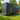 Portable container home on wheels in a grassy area with trees and a wooden fence in the background