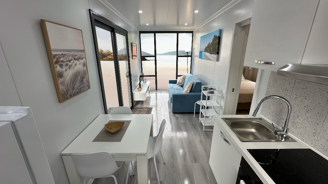 Stylish interior of JULIET 2 modular container home featuring kitchen, lounge, dining table, and full-height ocean view window